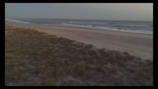 Low aerial tracking shot across and over sand dune to beach and ocean