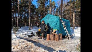 IN A WINTER TENT WITH A STOVE IN THE COLD -22 ° C. WINTER FOREST BY THE FROZEN RIVER.