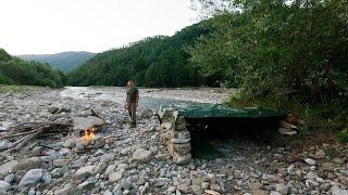 Building of a shelter made of stone near a mountain river, steak fried on fire