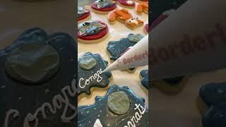 Cookie artist is piping the word Congrats on graduation cookies!