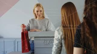 Friendly female cashier is taking garment from customer standing in line, asking her for payment