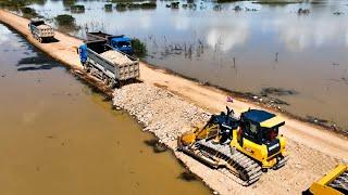 Strong Machinery Repairing Road On Water. Shantui Bulldozer And Large Dump Trucks Unloading Rock