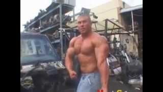 Blond bodybuilder flexing in auto yard